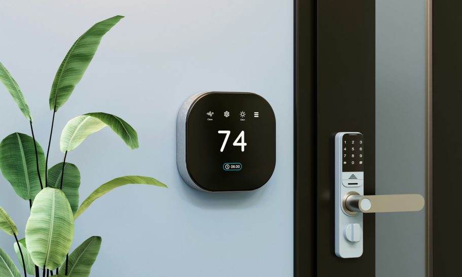Smart Home in Wesel installiert Schwarzes Thermostat an einer Wand, Temperaturanzeige 74, neben einer Pflanze und Türschloss.